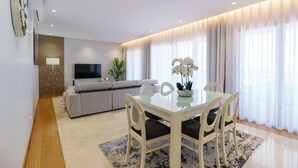 A modern living room with a dining area, a sofa, a flat-screen TV, and a large window with curtains. - MAR E SOL: The ultimate Madeira escape with stunning views and modern comforts! (Funchal)