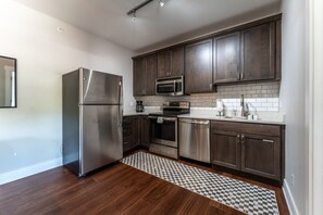 Een moderne keuken met donkere houten kastjes, roestvrijstalen apparatuur en een vloerkleed met een geruit patroon.