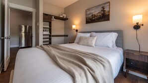 Ein Schlafzimmer mit einem Bett, einem Nachttisch, einer Wandlampe, einem Gemälde und einem Einbauschrank.