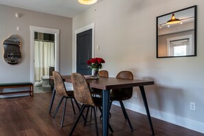Zona pranzo con tavolo, sedie, una panca, uno specchio e una porta che conduce al bagno.