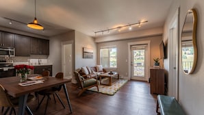 Eine moderne Küche mit dunklen Schränken, ein Essbereich mit Holztisch und Stühlen, ein Wohnzimmer mit Sofa und Couchtisch sowie ein Balkon mit Blick.