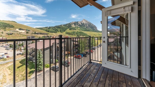 Ein Balkon mit Blick auf eine gebirgige Landschaft, ein Parkplatz und ein Gebäude mit einem Holzdach.