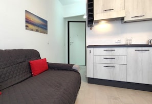 Um espaço compacto com cama, área de cozinha e porta para outro quarto.