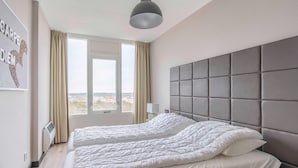 A hotel room with a large bed, a headboard, a window with curtains, and a wall-mounted air conditioner. - 4-person Apartment With Island View (De Koog)
