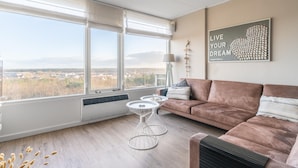 A modern living room with a large window, a brown sofa, two white wireframe tables, and a motivational poster on the wall. - 4-person Apartment With Island View (De Koog)