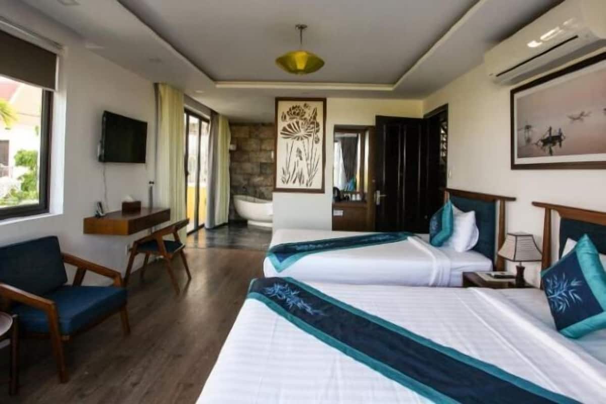 A hotel room with two beds, a TV, a desk, and a view of the outdoors.