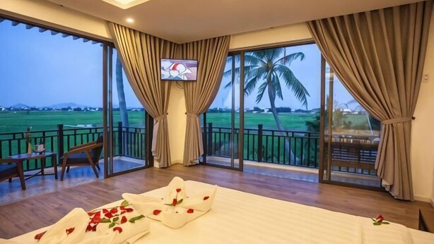 Une chambre d’hôtel comprenant un lit, une télévision, un balcon avec vue sur la campagne et un coin repas.