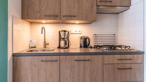 Une cuisine moderne avec des meubles en bois, un évier en acier inoxydable, une machine à café et une cuisinière à gaz.