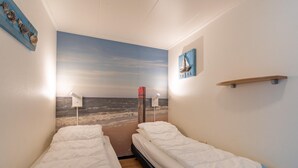 Une chambre avec deux lits, une fresque murale représentant une plage, une petite étagère et un interrupteur fixé au mur.