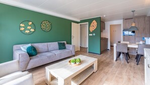 Un salon moderne avec un canapé, une table basse et des œuvres d’art murales. On aperçoit un coin cuisine à l’arrière-plan.