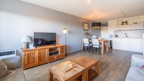 A modern living room with a sofa, wooden coffee table, and a TV. There is a dining area with chairs and a table, and a kitchen in the background. - Comfortable 4-person Apartment With Terrace and View (De Koog)