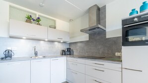 A modern kitchen with white cabinets, a stainless steel range hood, and a built-in oven. - Comfortable 4-person Apartment With Terrace and View (De Koog)