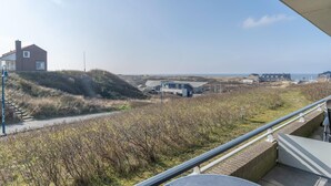 A coastal view with a house on a hill, a pathway, and a distant building. - Comfortable 4-person Apartment With Terrace and View (De Koog)