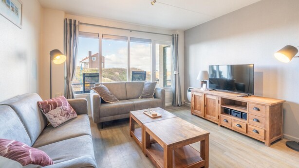 A modern living room with a sofa, coffee table, TV, and wooden cabinet. - Comfortable 4-person Apartment With Terrace and View (De Koog)