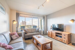 A modern living room with a sofa, coffee table, TV, and wooden cabinet. - Comfortable 4-person Apartment With Terrace and View (De Koog)
