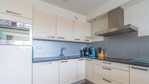 A modern kitchen with white cabinets, a Bosch oven, a stainless steel range hood, and a blue countertop. - 4-person Apartment With Island-sea View (De Koog)