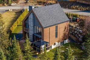 A modern house with a sloped roof, large windows, and a deck. - Boho Chic Lake Mountain Spa Games Kayak EV charger (Sainte-Lucie-des-Laurentides)