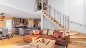Ein zeitgemäßer Wohnraum mit einer Holztreppe, einem Ledersofa und einer Küchenzeile.