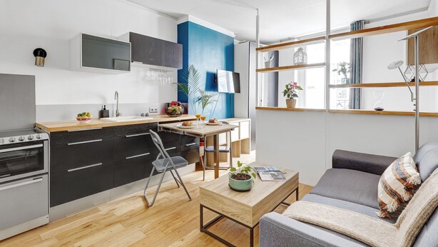 A modern kitchen with black cabinets, a wooden countertop, and a dining area with a table and chairs. - Cozy 1BR in Montorgueil (Paris)