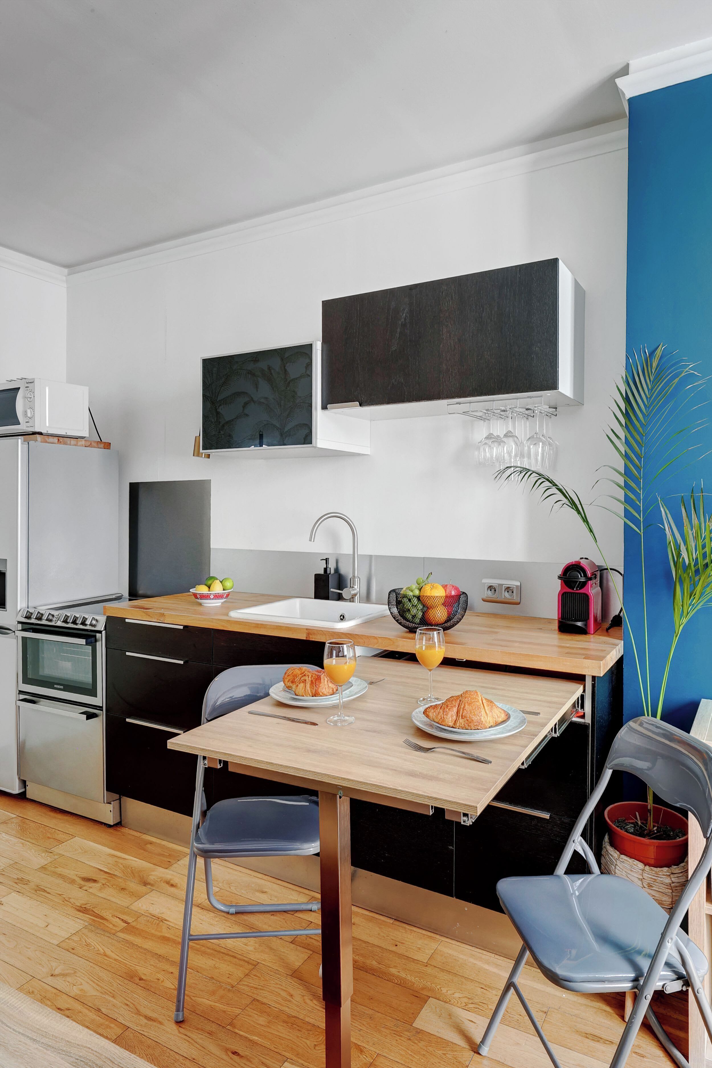 Une cuisine de taille réduite, avec une table en bois, deux chaises, un évier et un four à micro-ondes.