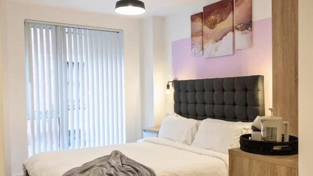 Une chambre à coucher avec un lit, une table de chevet, une lampe et des œuvres d’art accrochées au mur.