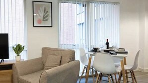 Un salon moderne avec un canapé beige, une table à manger avec des chaises blanches et une plante en pot.