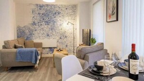 Un salon moderne avec un canapé, une table à manger dressée pour deux personnes et une bouteille de vin.