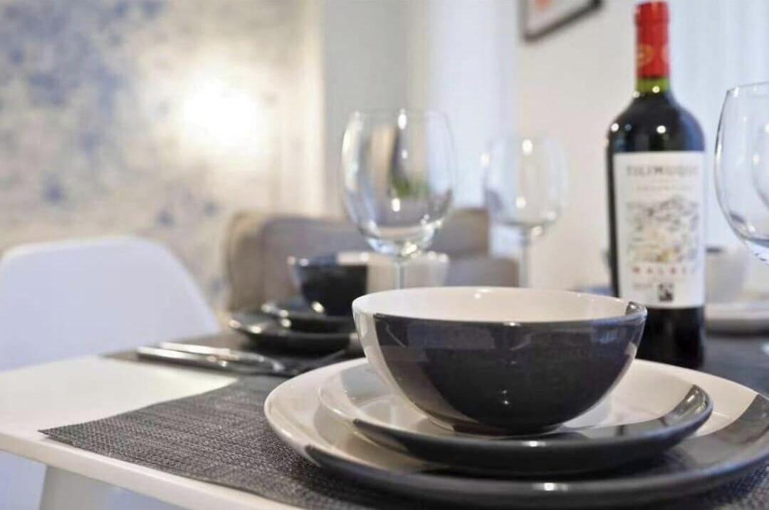 A dining table with a bowl and plates, a wine bottle, and glasses.