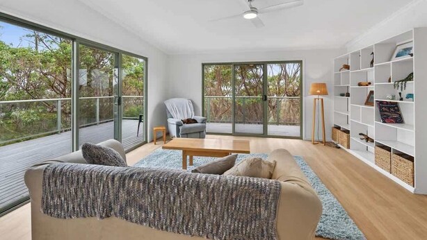 A modern living room with a sofa, a coffee table, and a bookshelf. - Kareelah | Ocean Views & Walk to Beach (Guerilla Bay)