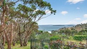 A coastal landscape with trees, a fence, and a view of the sea. - Kareelah | Ocean Views & Walk to Beach (Guerilla Bay)