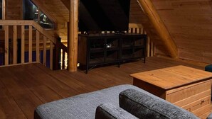 Ein gemütliches Schlafzimmer im Dachgeschoss mit Holzboden, einem Fernsehgerät auf einem Standfuß, einer Couch und einem kleinen Tisch.