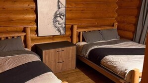 Ein schlicht eingerichtetes Schlafzimmer im Blockhausstil mit zwei Holzbetten, einem Nachttisch aus Holz und einem Bild eines Wolfes.