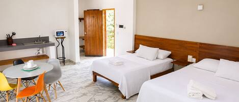 Habitación de hotel con dos camas, una kitchenette pequeña, una zona de comedor con sillas y un baño visible a través de una puerta abierta.