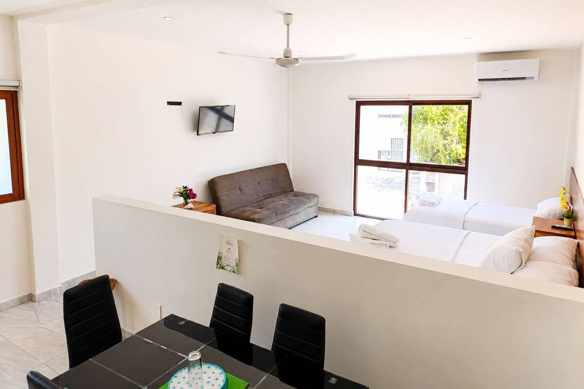 A modern hotel room with a balcony, a dining area, and a TV.
