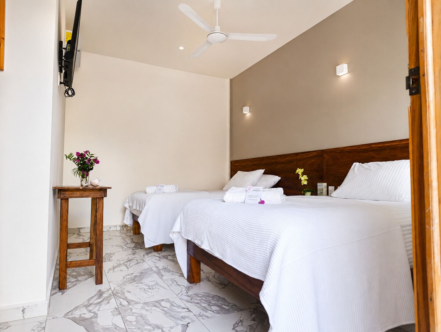 A hotel room with two beds, a wooden nightstand, a ceiling fan, and a marble floor.