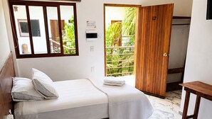 A room with two beds, a wooden door, a small table, and a window with a view of greenery. - Hotel Centrico Tulum (Tulum)