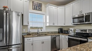 A modern kitchen with white cabinets, stainless steel appliances, and a granite countertop. - "Tailwinds and Tides" Ocean and Marsh Views on Holden Beach NC (Holden Beach)