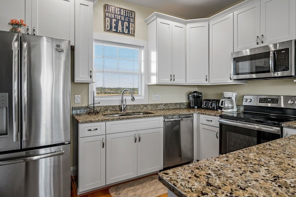 A modern kitchen with white cabinets, stainless steel appliances, and a granite countertop. - "Tailwinds and Tides" Ocean and Marsh Views on Holden Beach NC (Holden Beach)