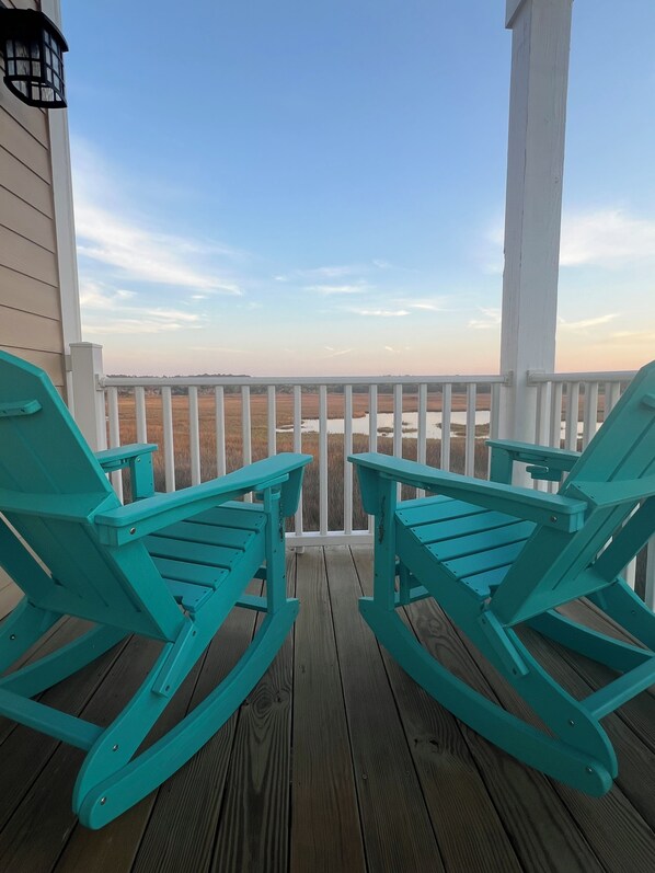 A wooden deck with two turquoise Adirondack chairs facing a view of a field and water. - "Tailwinds and Tides" Ocean and Marsh Views on Holden Beach NC (Holden Beach)