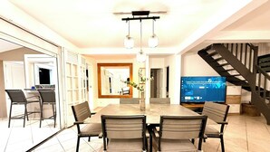 A modern dining area with a large table and chairs, a television, and a staircase.