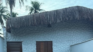 A building with a textured stone wall, a thatched roof, a wooden door, and a small window. - House on the beach street in Gostoso (Touros)