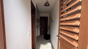 A narrow hallway with a wooden door on the right, a ceiling light, and a door at the end. - House on the beach street in Gostoso (Touros)
