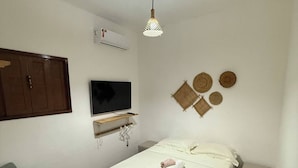 A small, clean room with a bed, a chair, a TV, and a hanging light fixture. - House on the beach street in Gostoso (Touros)
