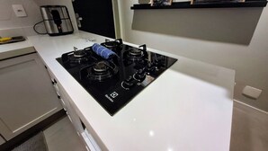 Une cuisine moderne avec un poêle noir, un plan de travail blanc et une petite étagère où sont exposées des photos encadrées.