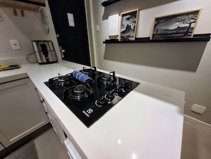 A modern kitchen with a black stove, white countertop, and a small shelf with framed pictures. - Leblon- Design e aconchego.  (Rio de Janeiro)