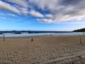 A beach with a volleyball net, a flag, and a sandy path leading to the water. - Leblon- Design e aconchego.  (Rio de Janeiro)