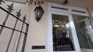 Une façade d’immeuble avec une adresse numérotée, un portail en métal, une fenêtre donnant sur un paysage et un luminaire fixé au mur.
