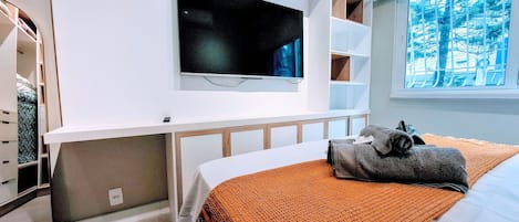 Et soveværelse med seng, tv ophængt på væggen, et vindue med udsigt og et klædeskab.