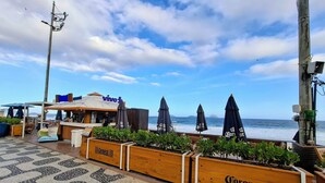 Un restaurant situé en bord de mer, avec une terrasse, une vue sur l’océan et des jardinières en bois ornées du logo Corona.