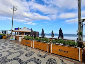 A beachside restaurant with outdoor seating, a view of the ocean, and wooden planters with the Corona logo. - Leblon- Design e aconchego.  (Rio de Janeiro)